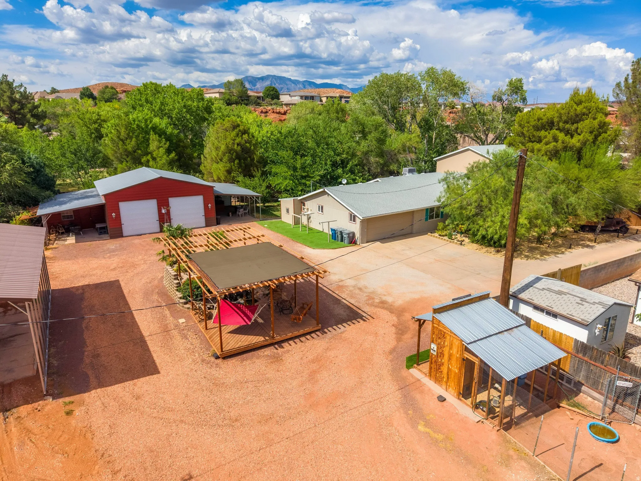 Spacious property featuring multiple structures, including a two-bay red barn with white garage doors, a main residence with a light-colored exterior, and an additional smaller structure with a natural wood finish and metal roof