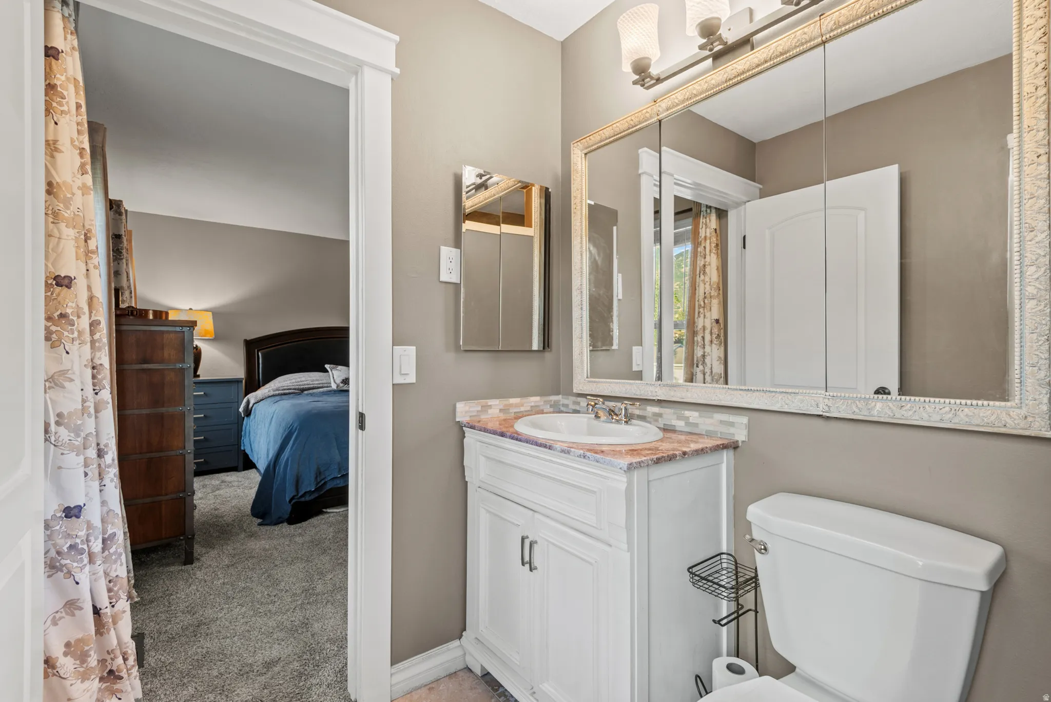 White vanity with integrated sink, patterned countertop, decorative framed medicine cabinet, and wall-mounted light fixture