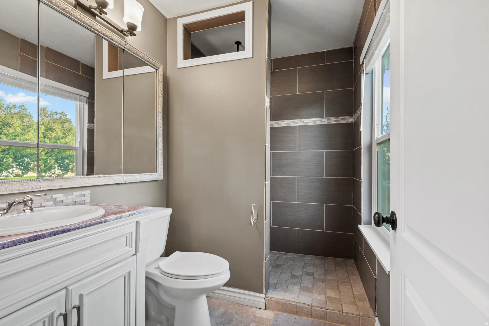Bathroom featuring a white vanity with an undermount sink, a framed medicine cabinet, and a shower with dark tiled walls and a mosaic accent band