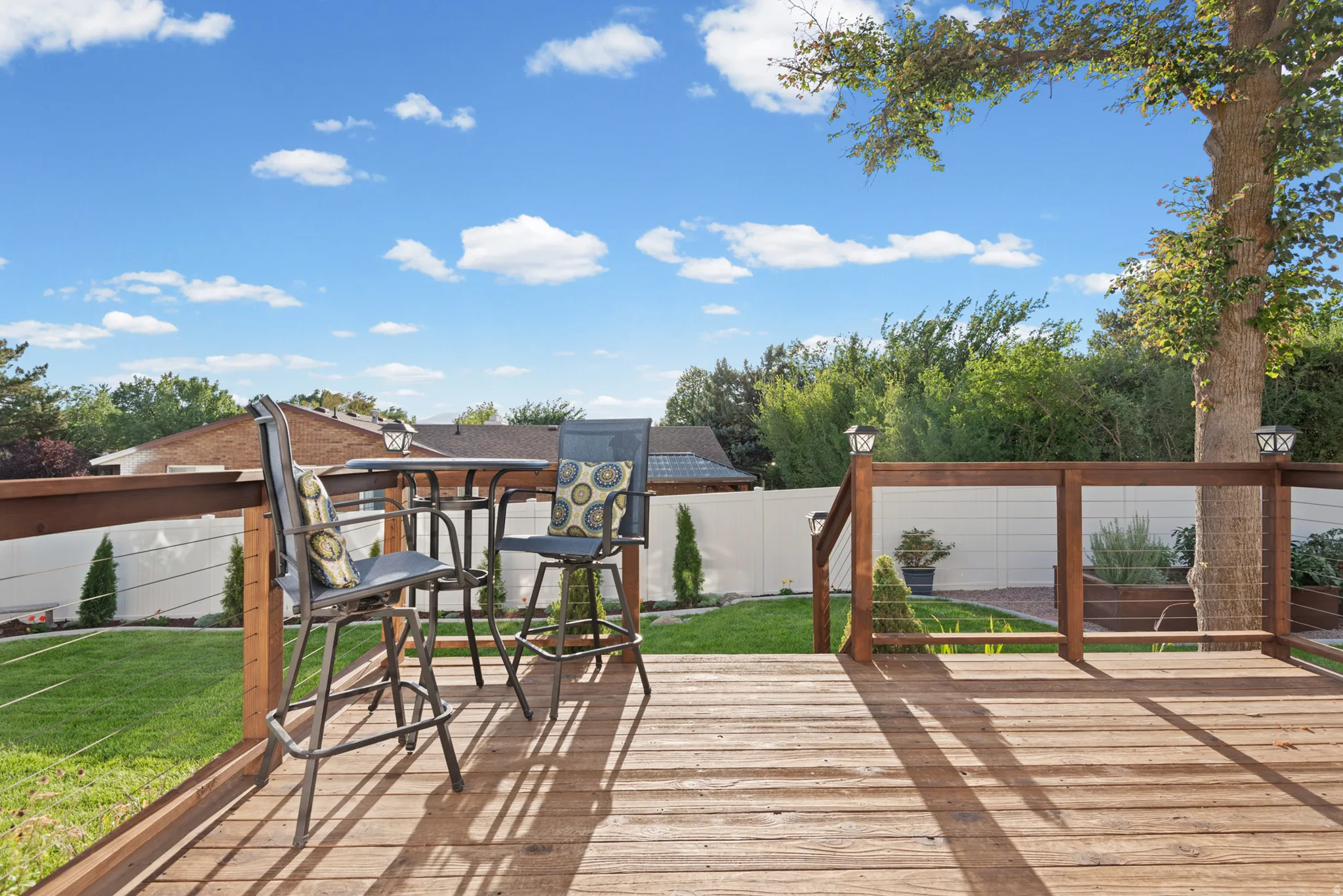 Expansive composite deck featuring warm wood-finish decking and integrated pergola structure with wooden beams, overlooking a professionally manicured lawn bordered by mature landscaping and privacy fencing