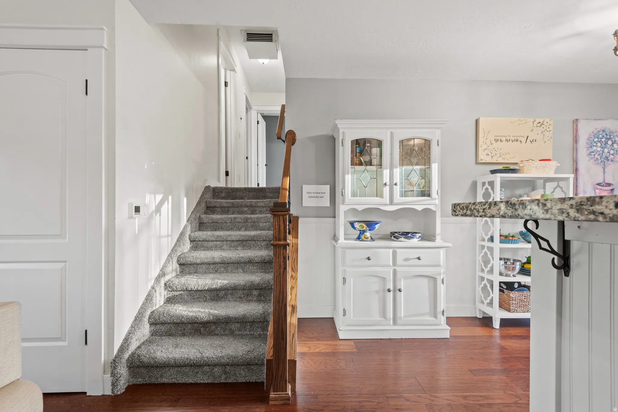Elegant foyer showcasing hardwood flooring, a carpeted staircase with wooden handrail, and white wainscoting
