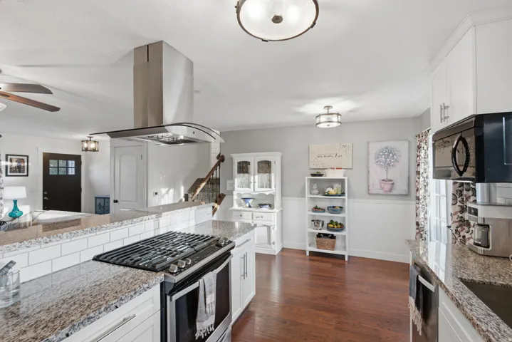 Chef's kitchen featuring white cabinetry with glass-front uppers, granite countertops, dual stainless steel appliances including a six-burner gas range and built-in refrigerator, a curved island with seating, and a stainless steel range hood