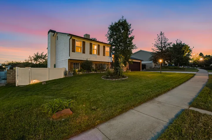 Split-level residence featuring a white vinyl exterior, brick accents, and a manicured front lawn with mature landscaping