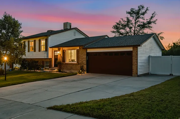 Two-story brick residence with illuminated interior spaces, featuring a dark-finish attached garage, concrete driveway, and manicured lawn with mature landscaping