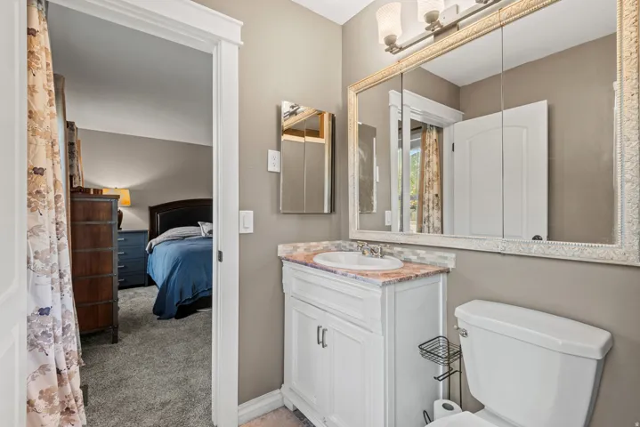 White vanity with integrated sink, patterned countertop, decorative framed medicine cabinet, and wall-mounted light fixture