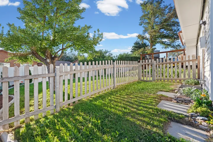Fenced backyard with mature shade trees, manicured lawn, and brick home exterior visible in background
