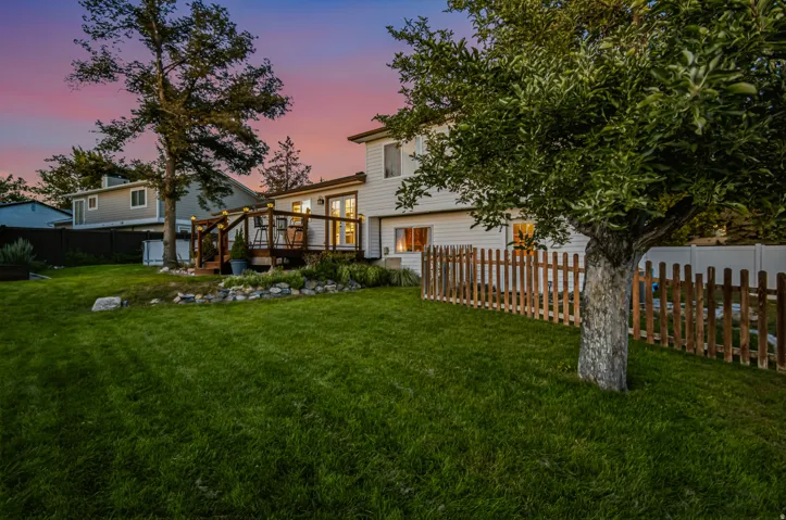 Expansive backyard featuring a manicured lawn, established landscaping, and a wooden deck