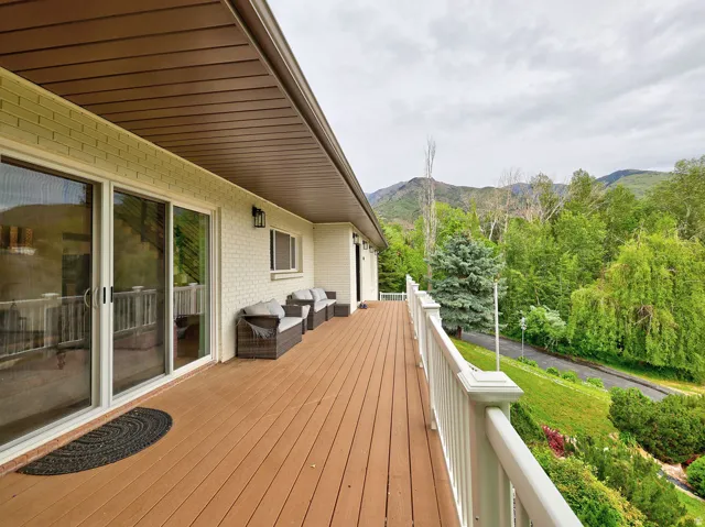 Expansive wood-finish deck with white railing, set against a backdrop of mature trees and distant mountains
