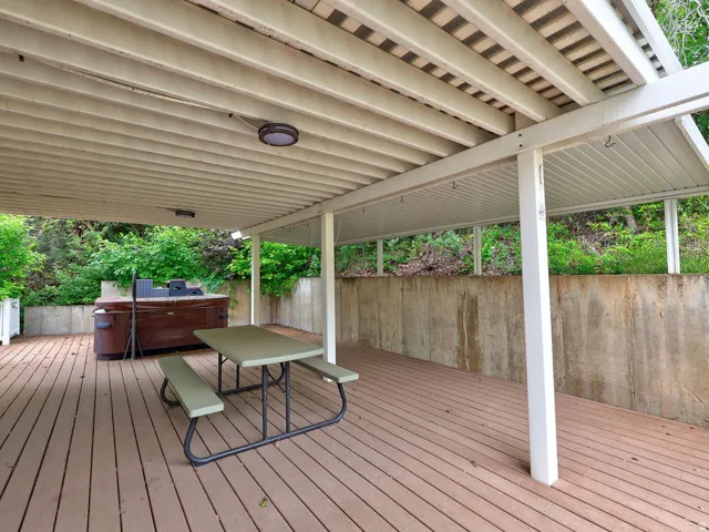 Expansive wood-finish deck featuring a slatted patio cover, two integrated ceiling lights, and a concrete retaining wall