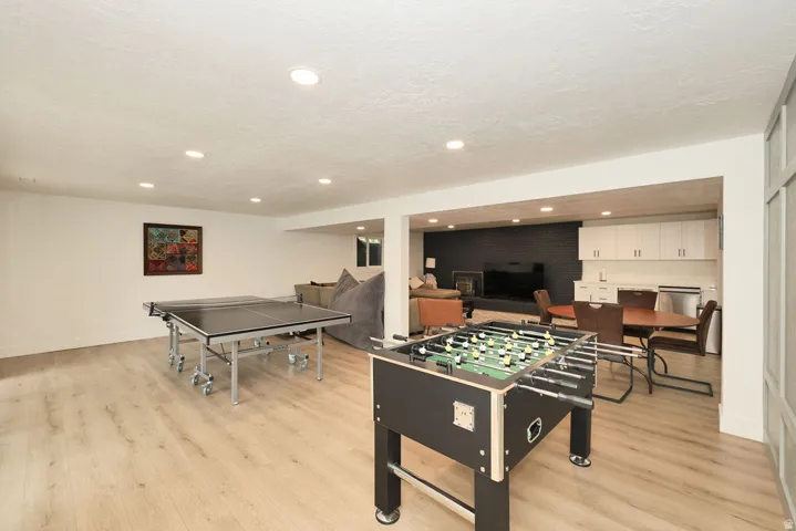 Expansive recreational space featuring recessed lighting, light wood-finish flooring, and a dedicated wet bar area with white cabinetry