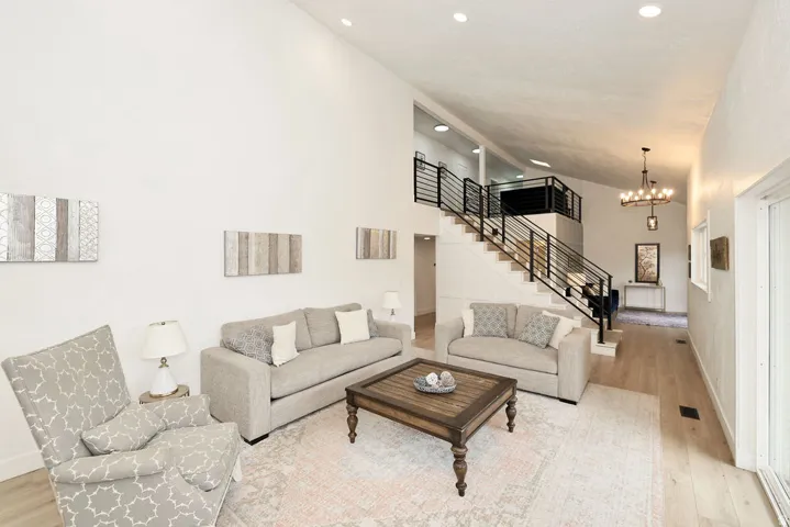 Spacious living area featuring high vaulted ceilings, light wood-finish flooring, a contemporary staircase with black metal railings, and recessed lighting