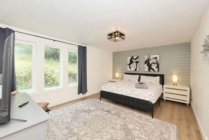 Bedroom featuring wood-finish flooring, a decorative accent wall, and a multi-pane window configuration