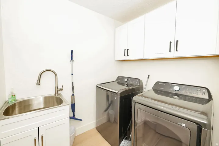 Dedicated laundry area featuring a utility sink with a gooseneck faucet, white cabinetry with dark pulls, and light wood-finish flooring