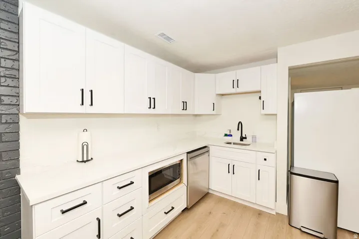 Contemporary kitchen featuring white cabinetry with black hardware, white countertops, a built-in microwave, and wood-finish flooring