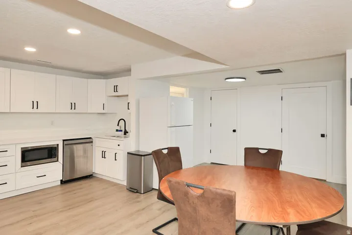Contemporary kitchen area featuring white cabinetry, light-toned wood-finish flooring, recessed lighting, stainless steel appliances, and a matte black faucet