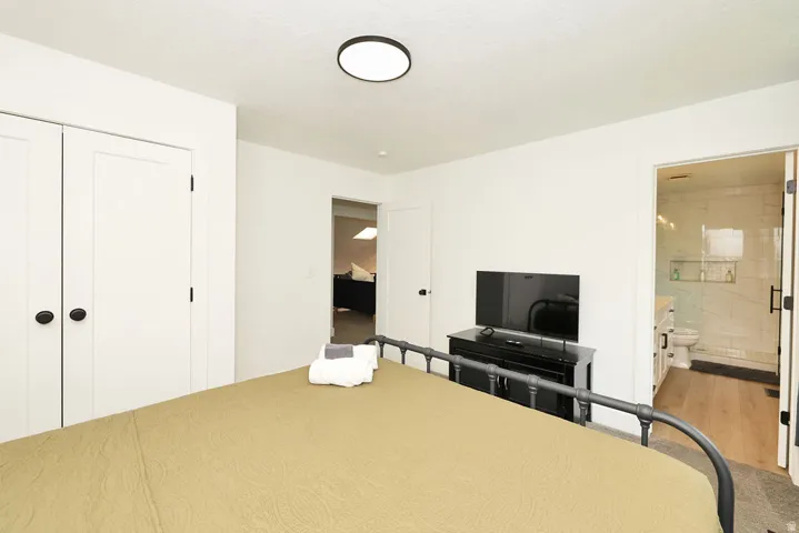 Bedroom featuring twin panel closet doors with black hardware, a round flush-mount ceiling light, and an en-suite bathroom entrance with a glass shower enclosure and wood-finish flooring