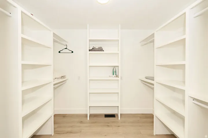 Customizable closet system with wood-finish flooring, white built-in shelving, and multiple hanging rods