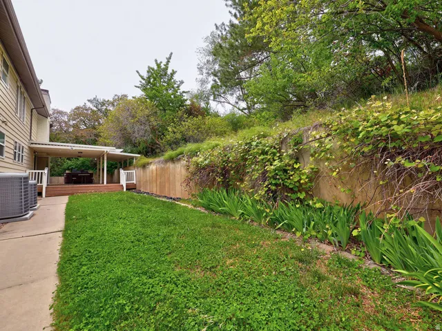 Expansive backyard featuring a covered patio, wood deck, and verdant hillside with established plantings