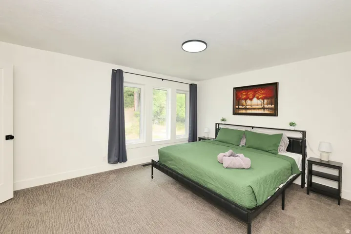Bedroom featuring three large windows with dark drapery, a flush-mount ceiling light, and textured carpet flooring