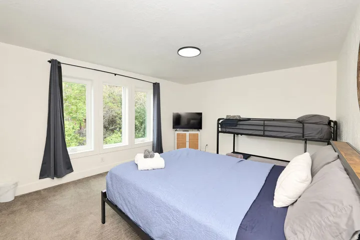 Bedroom featuring three large windows, a ceiling-mounted light fixture, and neutral carpeting