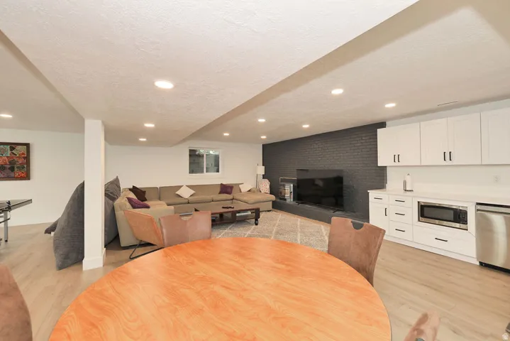 Spacious entertainment area featuring wood-finish flooring, recessed lighting, and a modern wet bar with white cabinetry, a built-in microwave, and stainless steel appliances