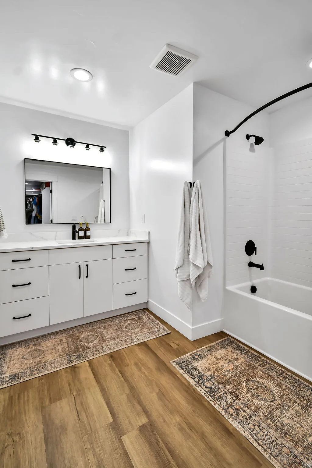 Contemporary bathroom featuring a white vanity with a light-toned countertop, black hardware, a black-framed mirror, and a black track light fixture