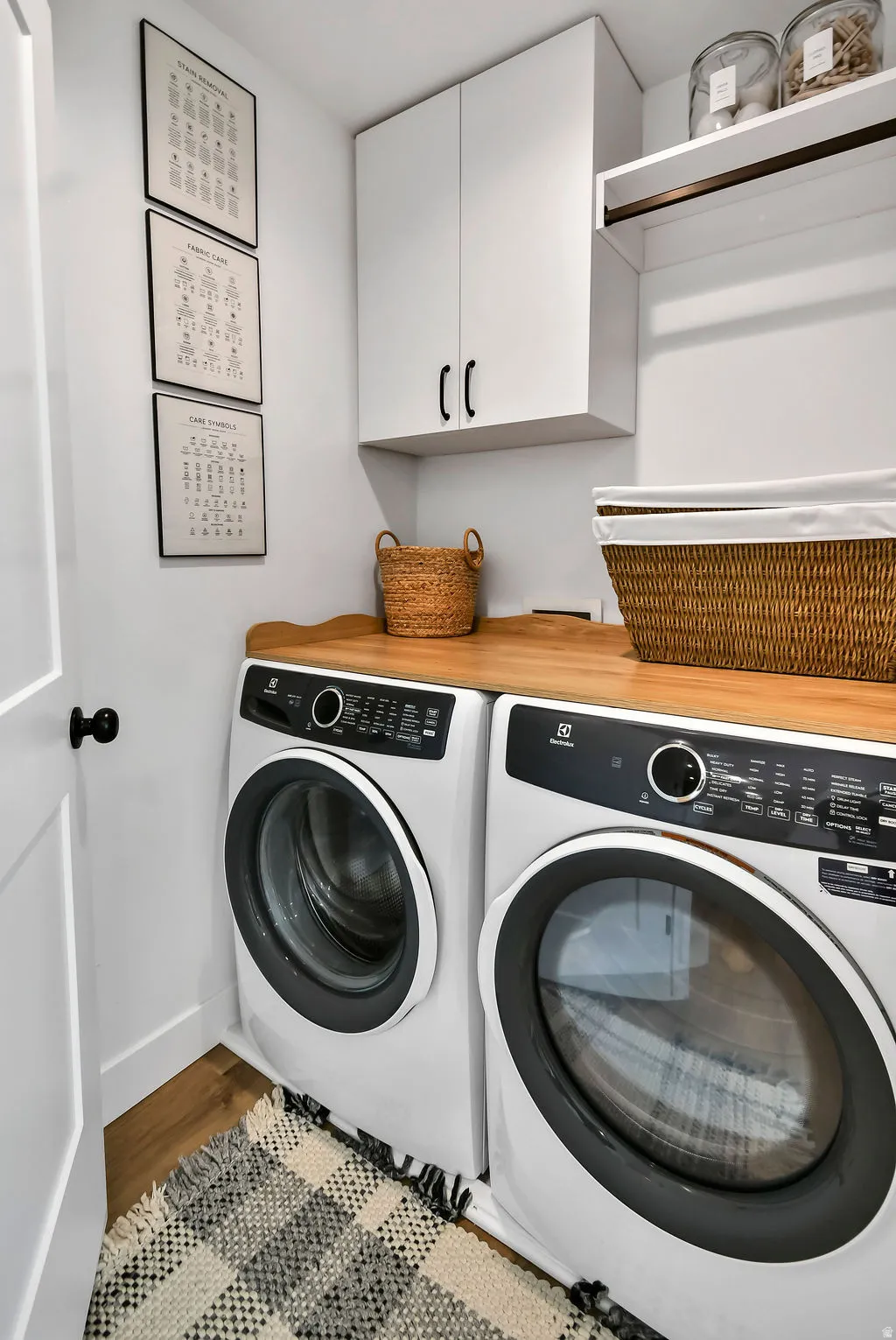 Dedicated laundry space featuring a wood-finish countertop, white cabinetry with dark hardware, and wood-finish flooring