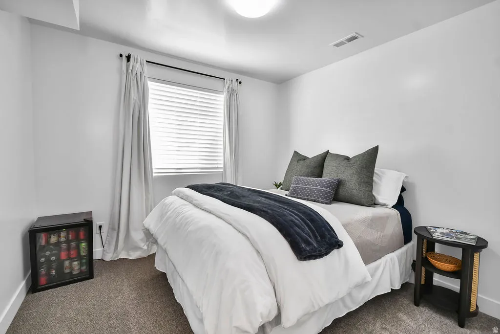 Bedroom featuring light gray carpet flooring, white walls, and a window with white blinds and drapes