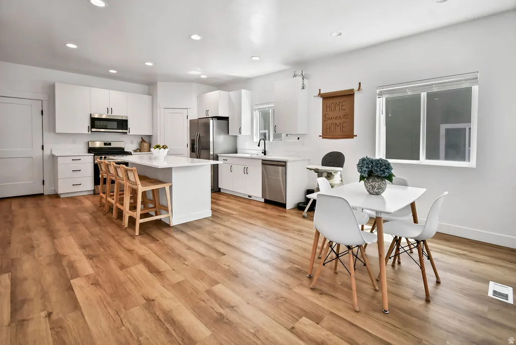 Spacious kitchen featuring an island with seating, white shaker cabinetry, stainless steel appliances, and wood-finish flooring