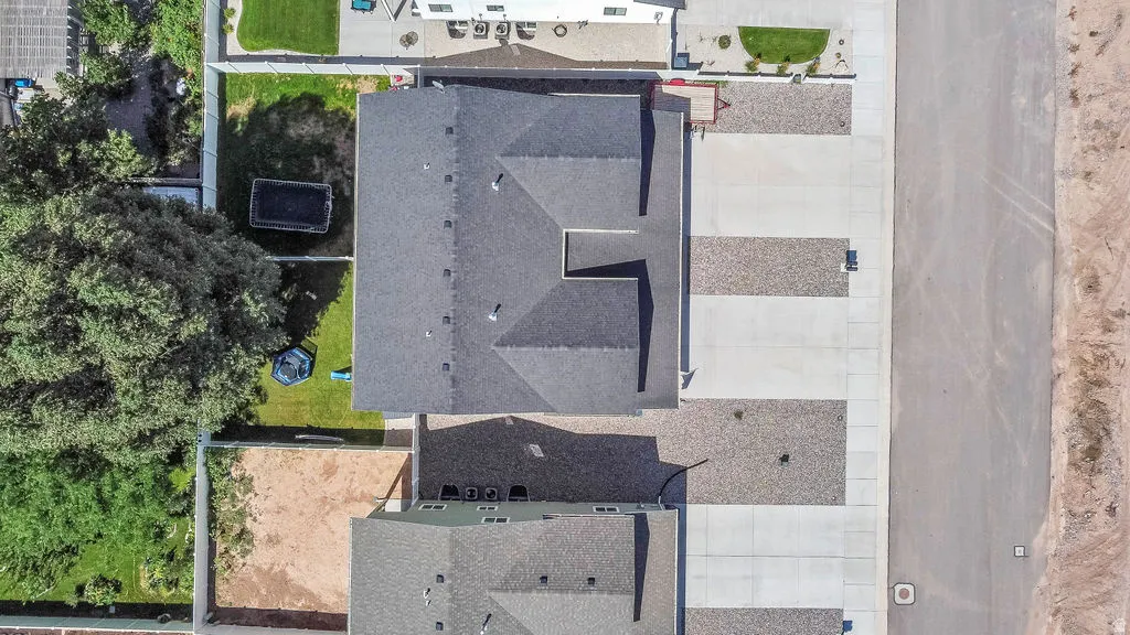 Aerial view showcasing a property with a dark shingle roof, a spacious concrete driveway, and an adjacent landscaped area featuring a vibrant green lawn
