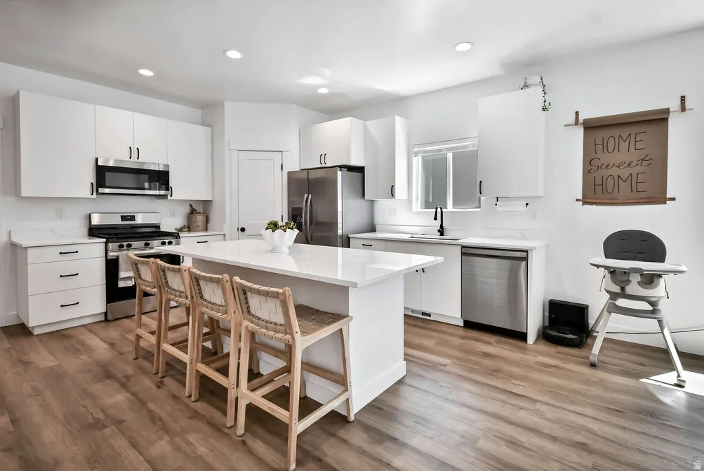 Bright kitchen featuring a central island with countertop seating, white cabinetry, stainless steel appliances, and wood-finish flooring