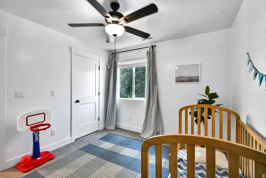 Bright room featuring a ceiling fan with integrated lighting, a white two-panel interior door with black hardware, a double-hung window, and grey wall-to-wall carpeting
