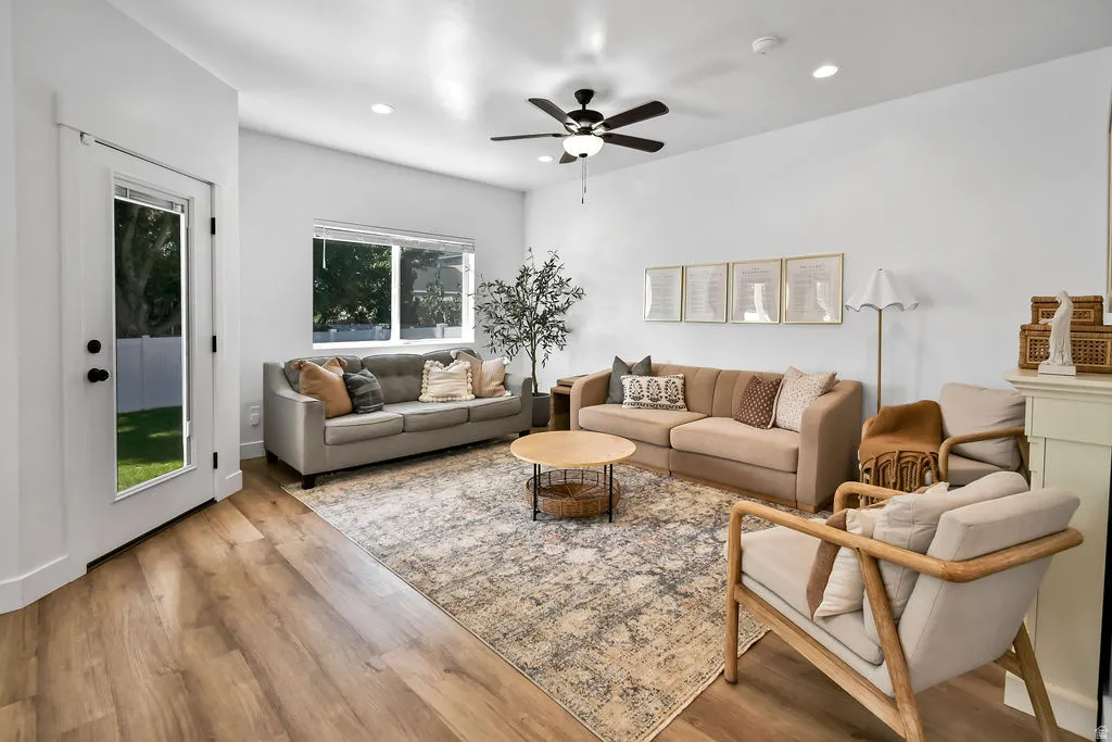 Open-concept living space with wood-finish flooring, a contemporary ceiling fan, recessed lighting, and a white-painted fireplace surround