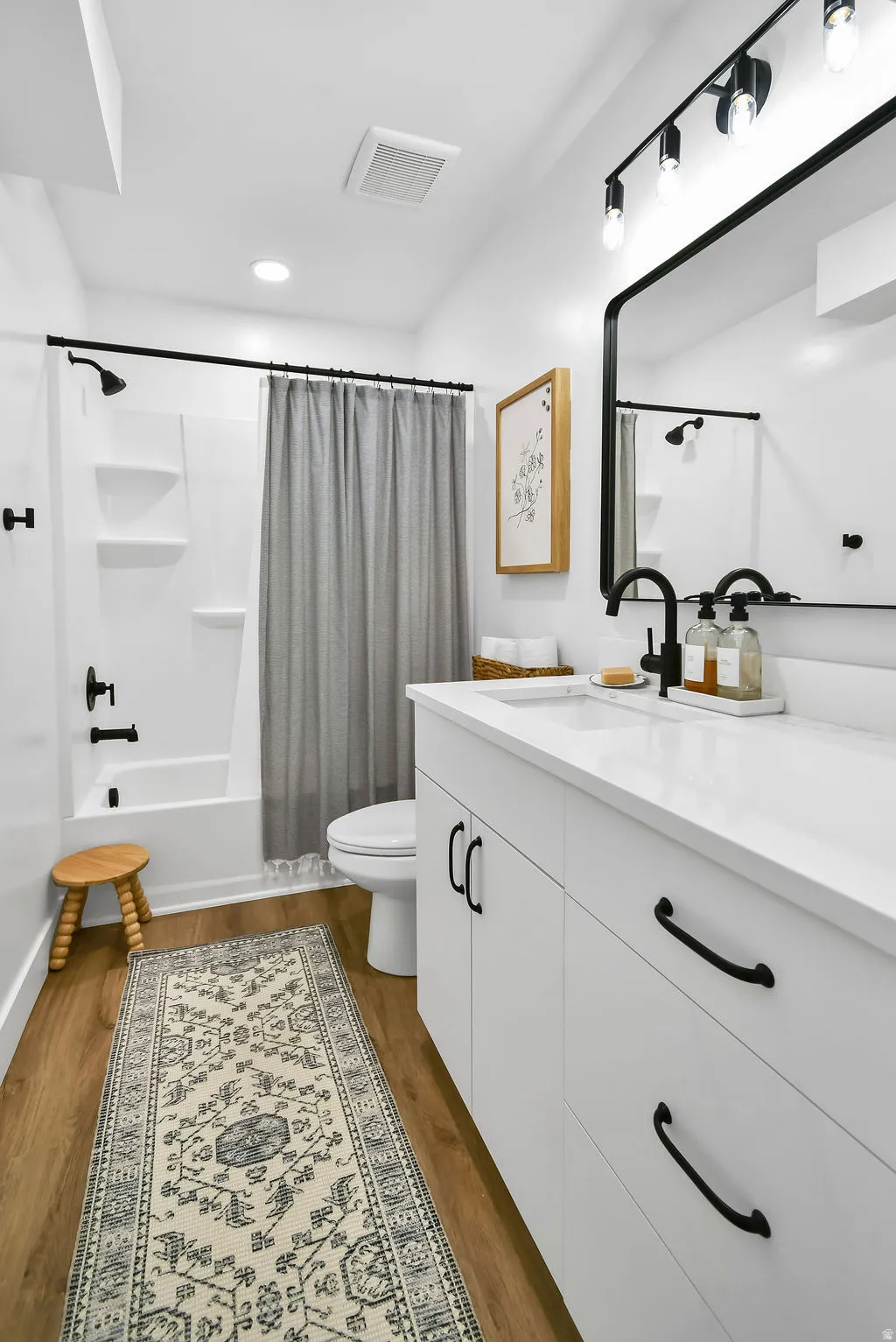 Contemporary bathroom featuring a white vanity with black hardware, an undermount sink, and wood-finish flooring