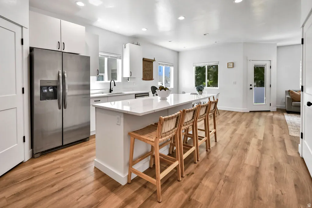 Modern kitchen featuring wood-finish flooring, white cabinetry, stainless steel appliances, a large center island with seating, and ample natural light from multiple windows