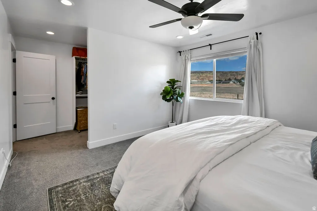 Carpeted bedroom featuring a large window with distant land scenery, a ceiling fan with integrated lighting, recessed lighting, and a closet with a solid panel door