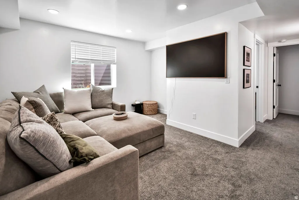 Spacious living area featuring neutral-toned carpeting, recessed lighting, and a window with horizontal blinds