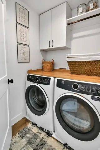 Dedicated laundry space featuring a wood-finish countertop, white cabinetry with dark hardware, and wood-finish flooring