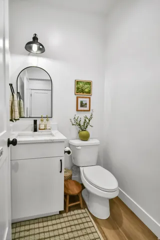 Powder room featuring a white single-sink vanity with a quartz countertop, a black arched mirror, and wood-finish flooring