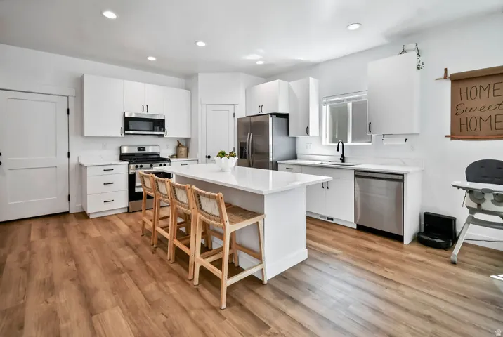 Contemporary kitchen featuring an expansive center island, white cabinetry, integrated stainless steel appliances, wood-finish flooring, and recessed lighting