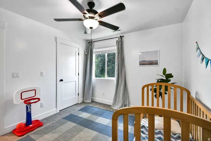 Bright room featuring a ceiling fan with integrated lighting, a white two-panel interior door with black hardware, a double-hung window, and grey wall-to-wall carpeting