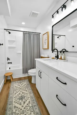 Contemporary bathroom featuring a white vanity with black hardware, an undermount sink, and wood-finish flooring