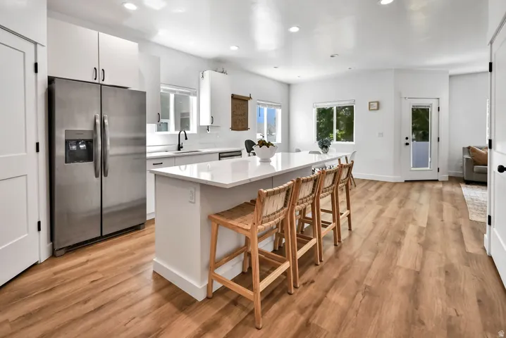 Modern kitchen featuring wood-finish flooring, white cabinetry, stainless steel appliances, a large center island with seating, and ample natural light from multiple windows