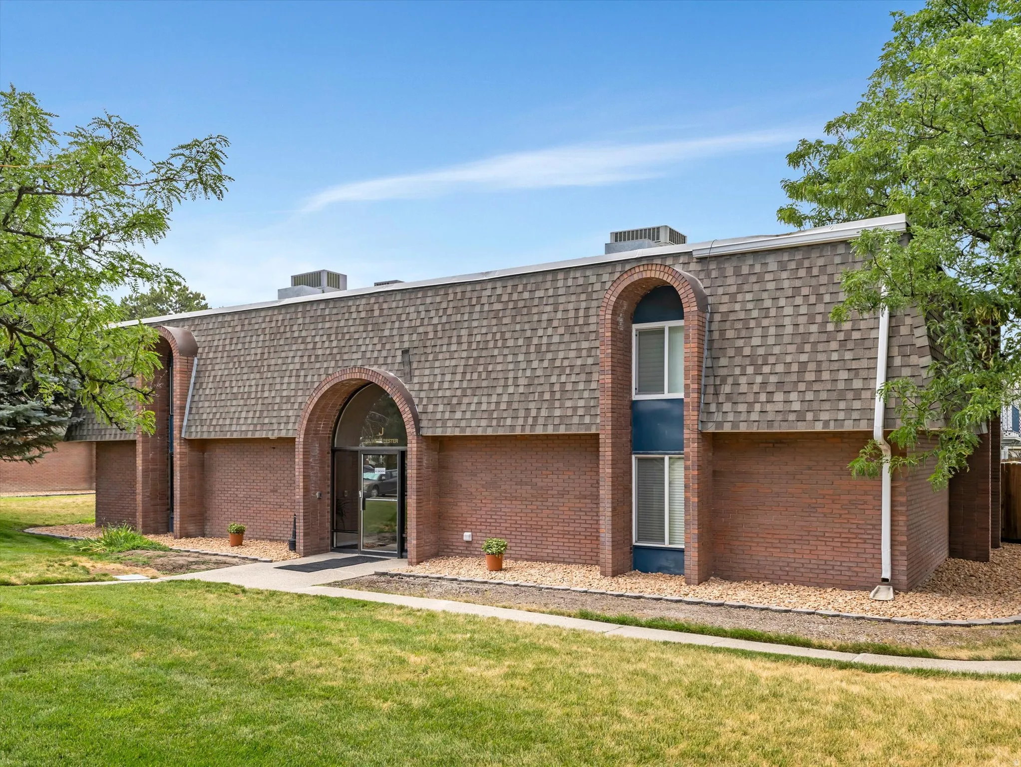 Brick exterior with a mansard roof, arched entryway, and mature landscaping