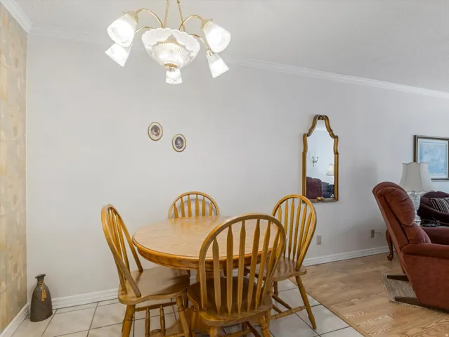 Dining area with a gold-tone chandelier, crown molding, and tiled flooring