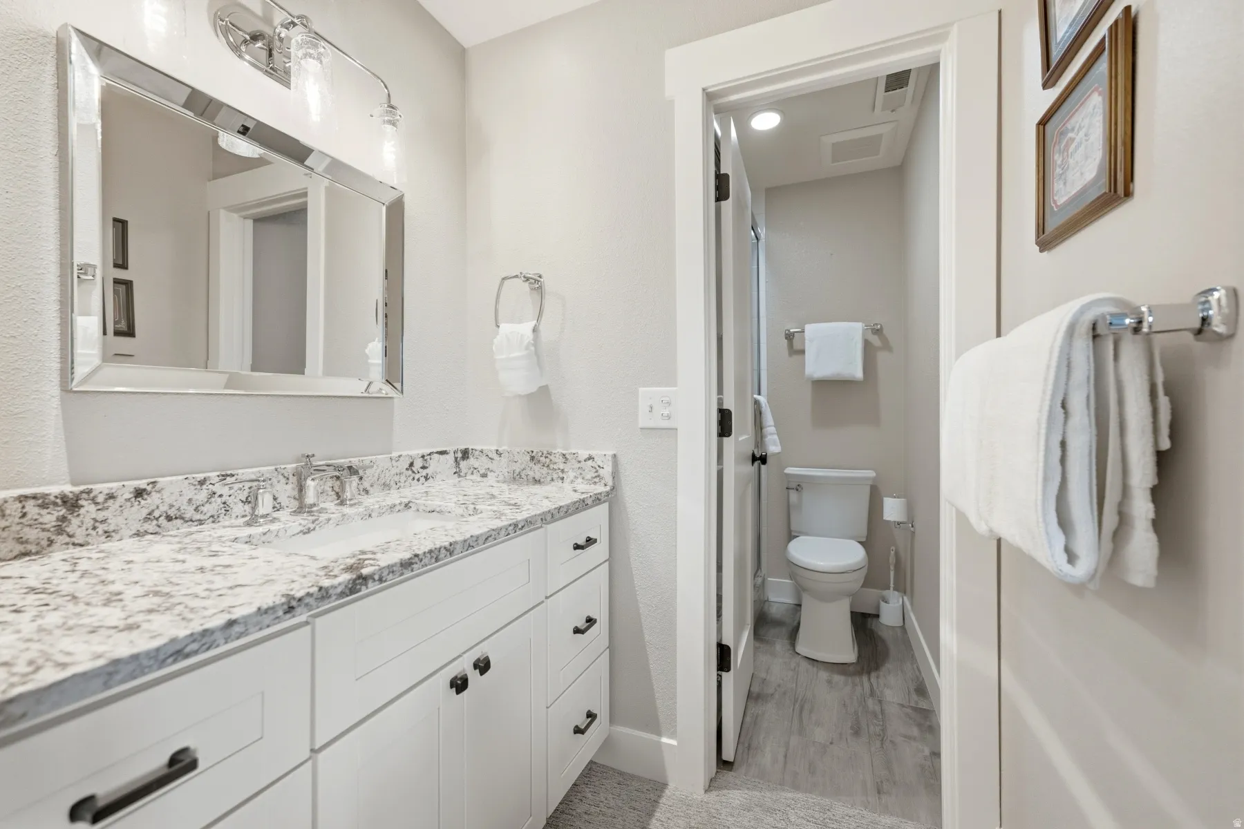 White shaker-style vanity with a granite countertop, undermount sink, and chrome faucet