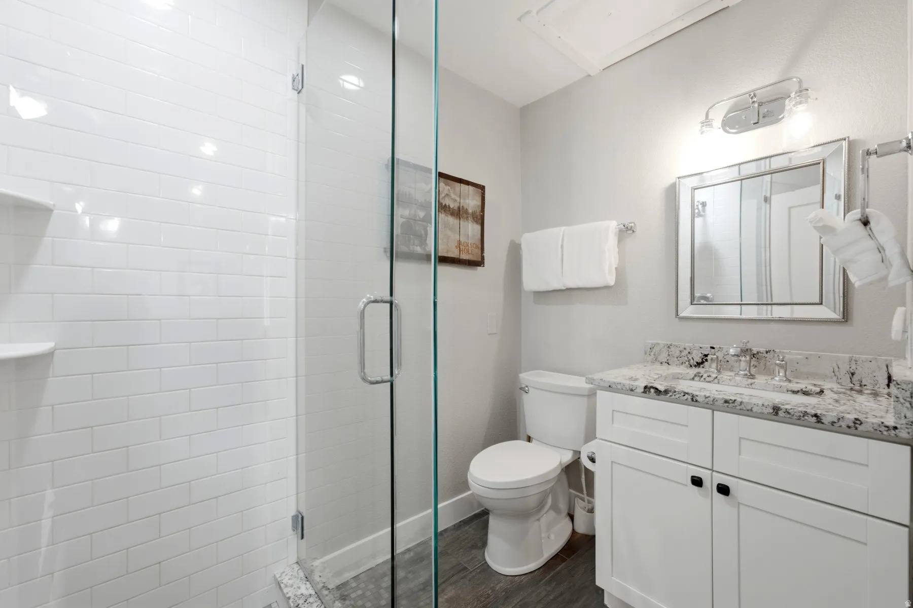 Contemporary bathroom featuring a frameless glass shower enclosure, white subway tile shower surround, and wood-finish flooring