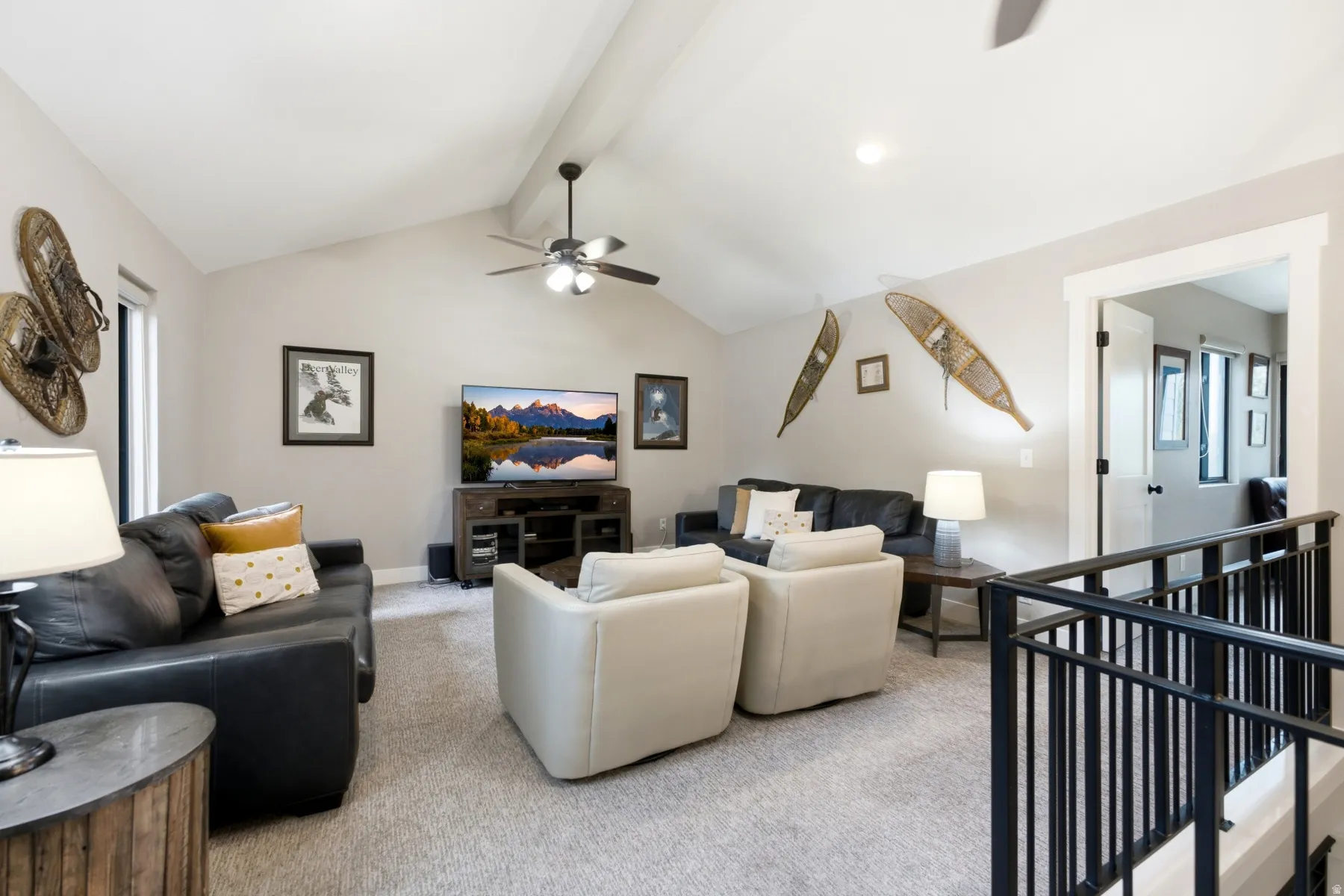 Spacious living area featuring a vaulted ceiling with a ceiling fan, light-toned carpeting, and an open doorway with white trim