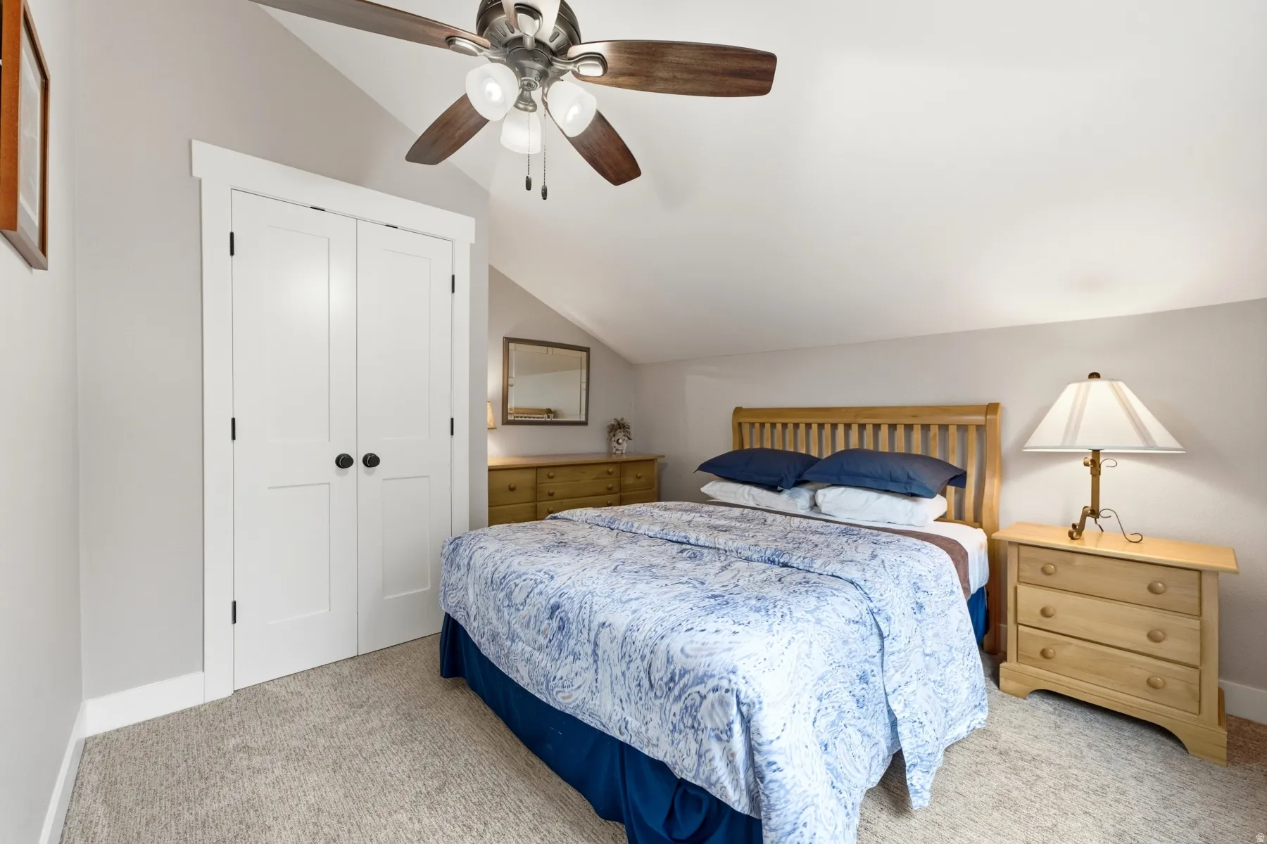 Carpeted room with a ceiling fan, sloped ceiling, double closet doors, and light-toned walls