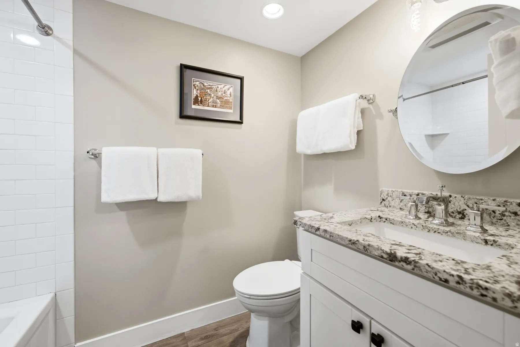 Bathroom featuring a white vanity with a speckled countertop, a round mirror, and a white subway tile shower surround